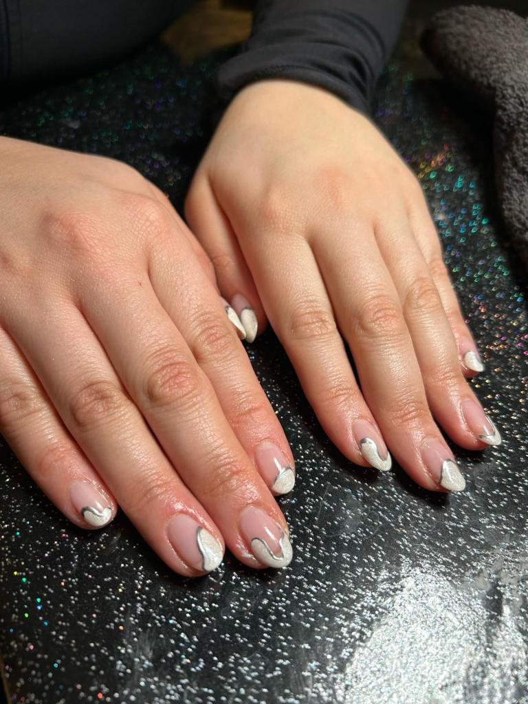 Close-up of well-manicured hands with white and silver nail art on a glittery black surface.