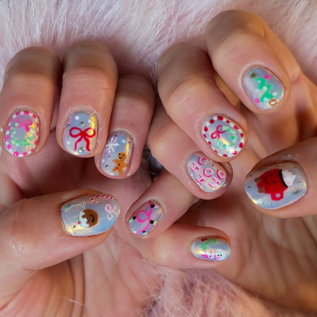 Close-up of hands with colorful Christmas-themed nail art, featuring designs like gingerbread men, candy canes, and festive ribbons on a shimmery background.